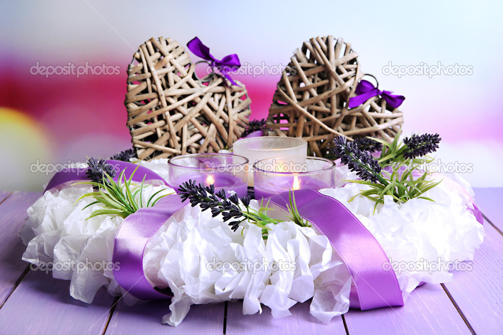 Decorative wreath with candles and wicker heats on table on bright background