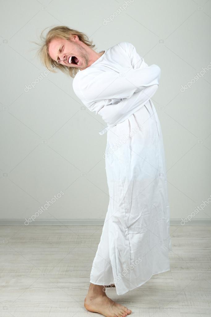 Mentally ill man in strait-jacket on gray background