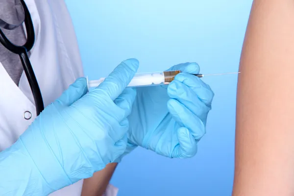 Doktor holding şırınga ile mavi arka plan üzerinde hastanın omuz içine aşı — Stok fotoğraf