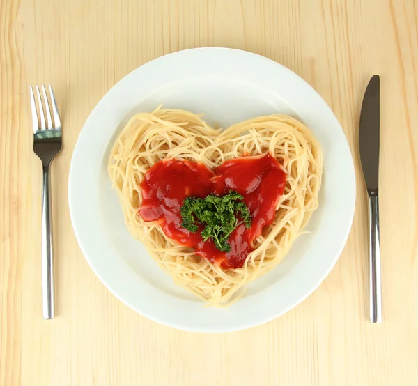 Gotowane spaghetti starannie ułożone w kształcie serca i polane sosem pomidorowym, na tle drewniane — Zdjęcie stockowe