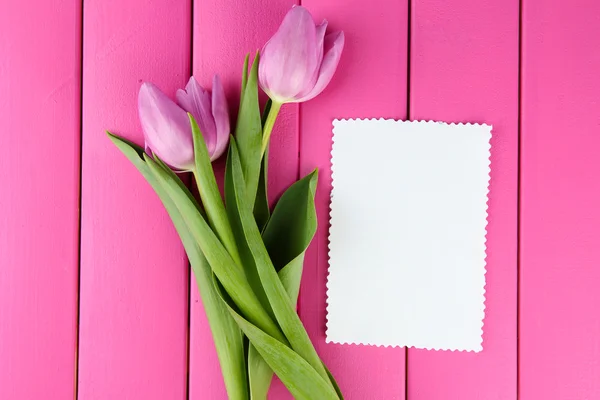 Gyönyörű csokor lila tulipán és üres kártya rózsaszín fából készült háttér — Stock Fotó