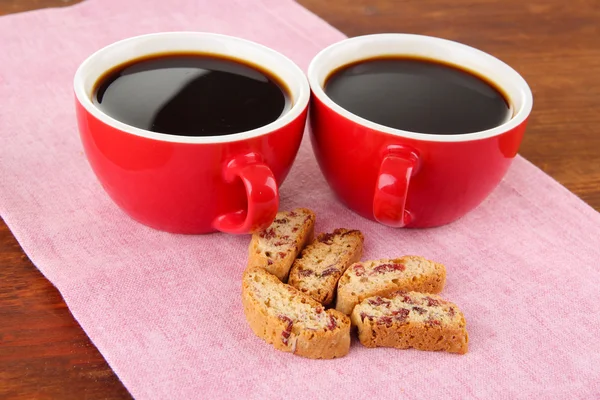 Red cups of strong coffee and cookies on napkin on wooden background — Stock Photo, Image