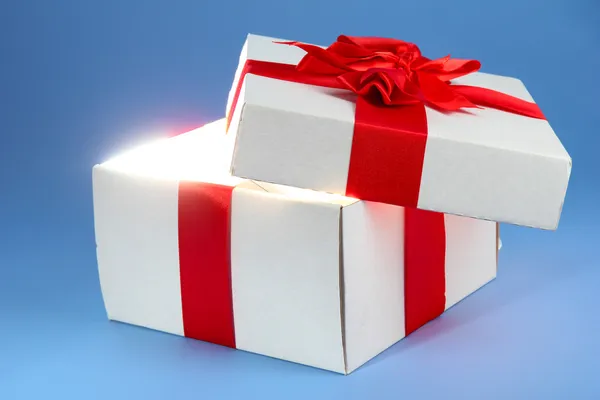 Gift box with bright light on it on blue background — Stock Photo, Image