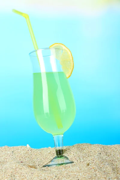 Beach cocktail in sand on blue background — Stock Photo, Image