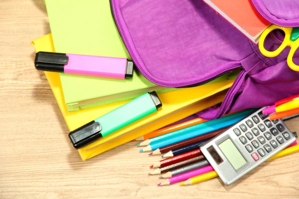 Purple backpack with school supplies on wooden background — Stock Photo, Image