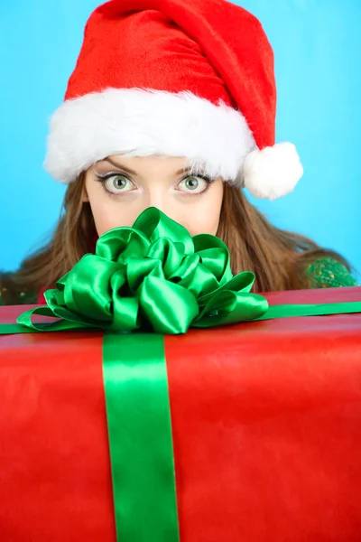 Schönes lächelndes Mädchen in Neujahrsmütze mit Geschenk auf blauem Hintergrund — Stockfoto