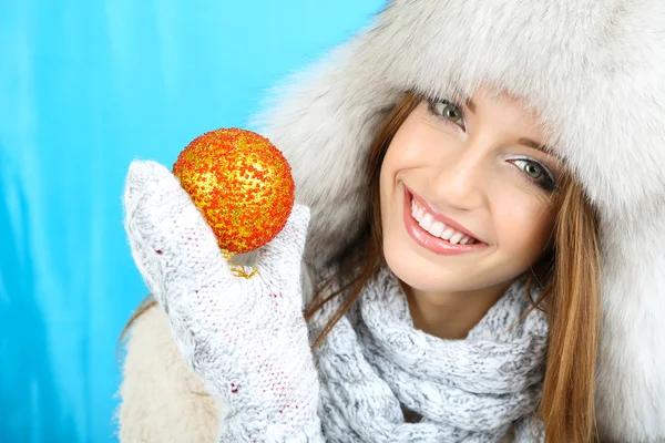 Hermosa chica sonriente con bola de Navidad sobre fondo azul — Foto de Stock