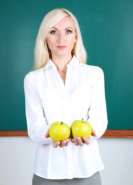 School teacher near blackboard with apples in classroom