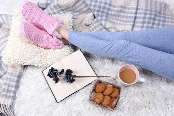 Composición con cuadros calientes, libro, taza de bebida caliente y piernas femeninas, sobre fondo de alfombra de color — Foto de Stock