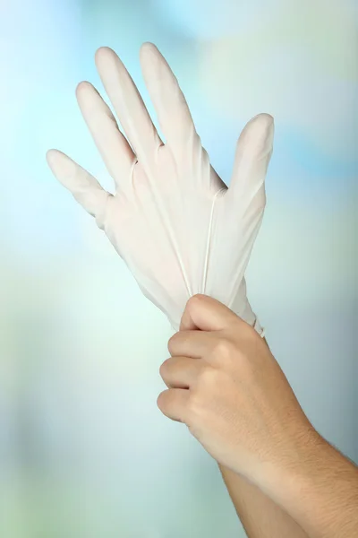 Médico poniéndose guantes protectores, sobre fondo claro — Foto de Stock