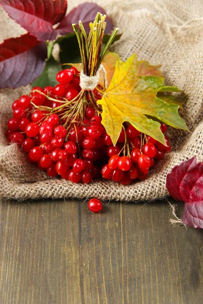 Red berries of viburnum on sackcloth napkin, on wooden background — Stock Photo, Image