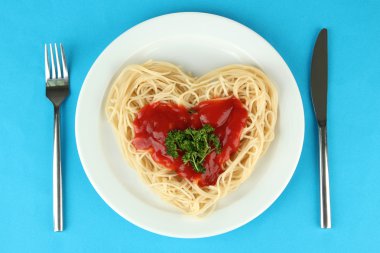 dikkatli bir şekilde kalp şeklinde düzenlenmiş ve renkli arka plan üzerinde domates soslu tepesinde pişmiş spagetti