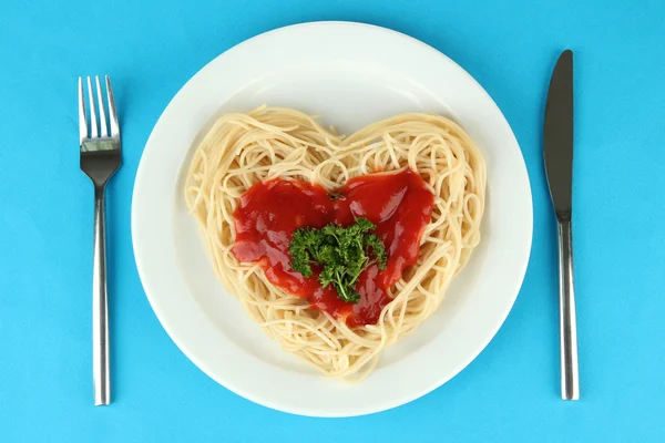 Spaghettis cuits soigneusement disposés en forme de coeur et garnis de sauce tomate, sur fond de couleur — Photo