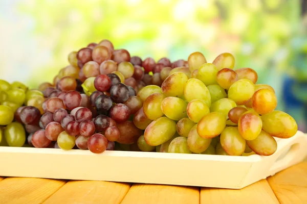 Свежий виноград на деревянном подносе на ярком фоне — стоковое фото