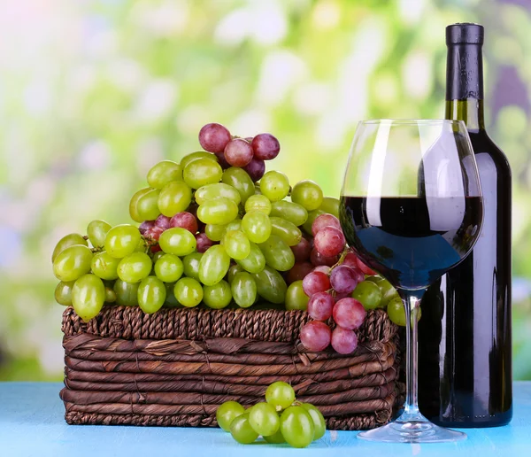 Ripe green and purple grapes in basket with wine on wooden table on natural background — Stock Photo, Image