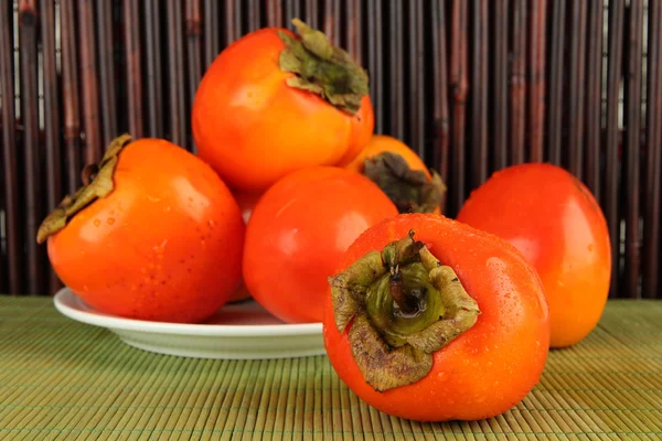 Ripe persimmons on plate on table on bamboo background — Stock Photo, Image