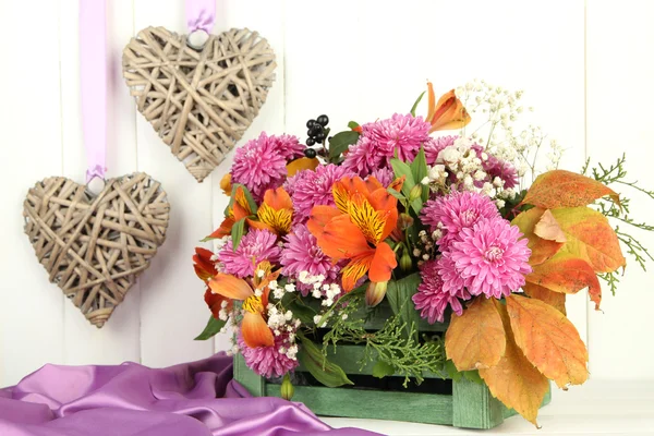 Flowers composition in crate with decorative hearts on table on wooden background — Stock Photo, Image