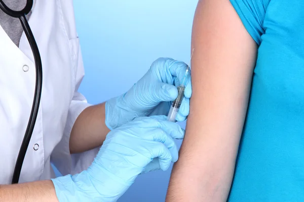 Lekarz gospodarstwa strzykawka szczepionki na ramię pacjenta na niebieskim tle — Zdjęcie stockowe