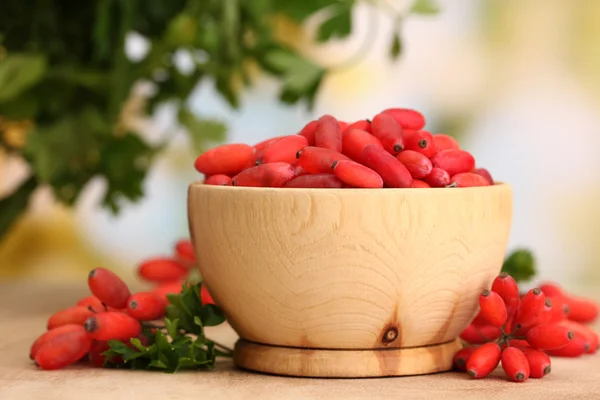Спелые ягоды в деревянной чаше с зелеными листьями, на столе — стоковое фото