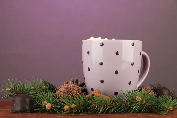 Cup of hot cacao with chocolates and fir branches on table on dark background