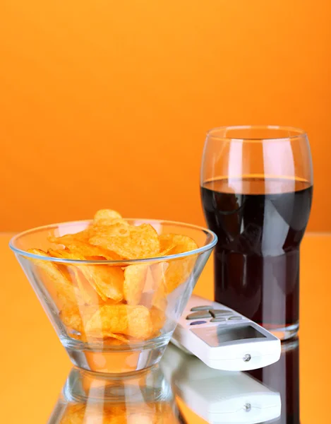 Chips in bowl, cola and TV remote on orange background — Stock Photo, Image