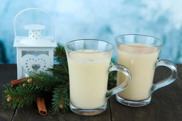 Cups of eggnog with fir branches and lantern on table on bright background — Stock Photo, Image