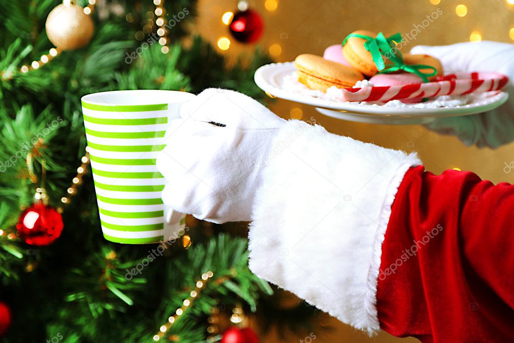 Santa holding mug and plate with cookies in his hand, on bright background
