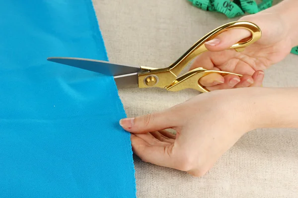 Seamstress cut blue fabric on beige fabric background — Stock Photo, Image