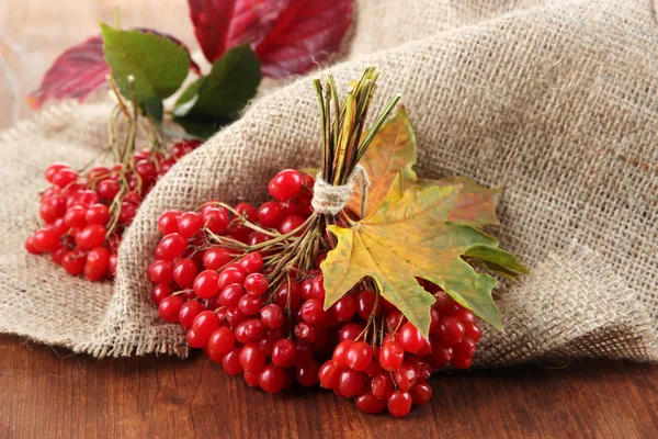 Red berries of viburnum on sackcloth napkin, on wooden background — Stock Photo, Image