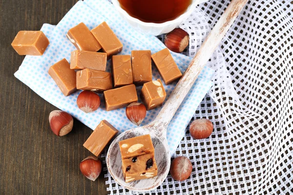 Many toffee in spoon and cup of tea on napkins on wooden table — Stock Photo, Image