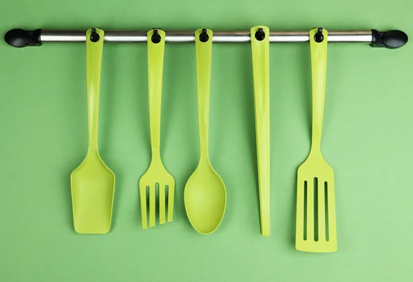 Plastic kitchen utensils on silver hooks on green background — Stock Photo, Image