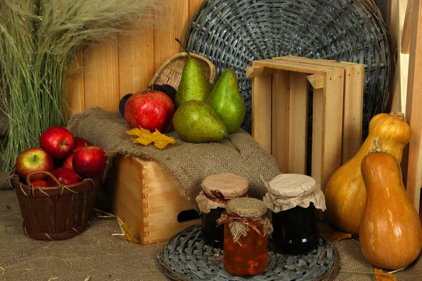 Vruchten op krat met potje jam en pompoenen op rouwgewaad op houten achtergrond — Stockfoto