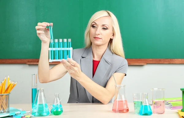 Chemistry teacher with tubes sitting at table on blackboard background — Stock Photo, Image