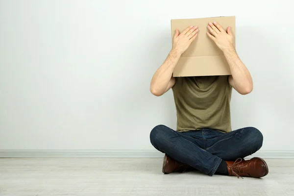 Hombre con caja de cartón en la cabeza sentado en el suelo cerca de la pared — Foto de Stock