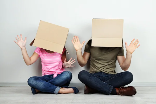 Casal com caixas de papelão em suas cabeças sentado no chão perto da parede — Fotografia de Stock