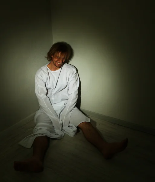 Mentally ill man in strait-jacket in room corner - Stock Photo, Image. 