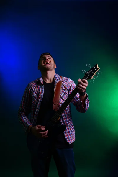 Young musician playing guitar and singing, on dark color background — Stock Photo, Image
