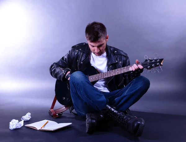 Jovem músico tocando guitarra em fundo cinza — Fotografia de Stock