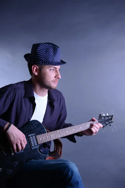 Young musician playing acoustic guitar and singing, on gray background — Stock Photo, Image