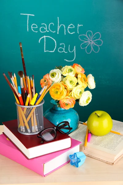 School supplies and flowers on blackboard background with inscription Teacher Day — Stock Photo, Image