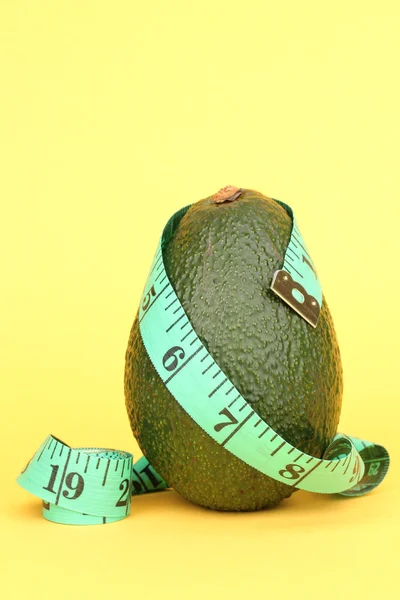 Avocado with measuring tape on yellow background — Stock Photo, Image