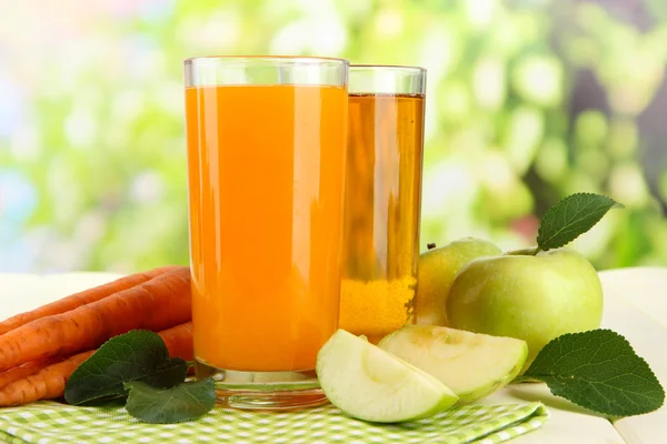 Окуляри з соку, яблук і моркви на білому дерев'яному столі, на зеленому фоні — стокове фото