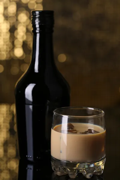 Baileys liqueur in bottle and glass on golden background — Stock Photo, Image