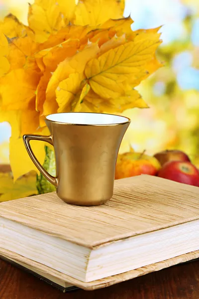 Autumn leaves, cup and book on wooden table on natural background — Stock Photo, Image