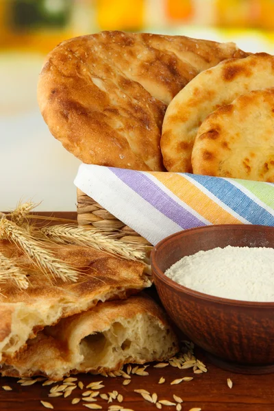 Pita breads in basket with spikes and flour on table on bright background — Stock Photo, Image