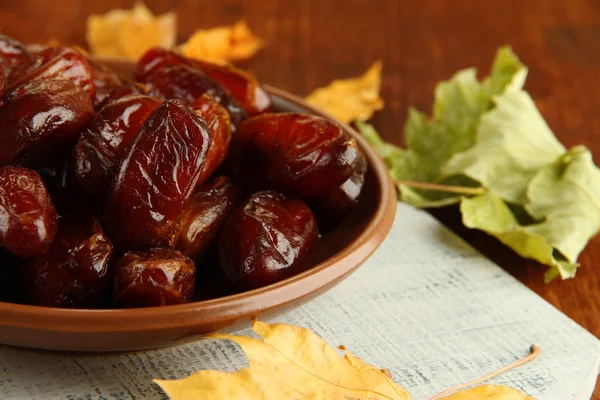 Dried dates on plate with yellow leaves on wooden background — Stock Photo, Image