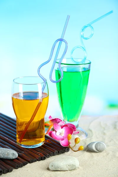 Glasses of cocktails on sand, on bright background — Stock Photo, Image