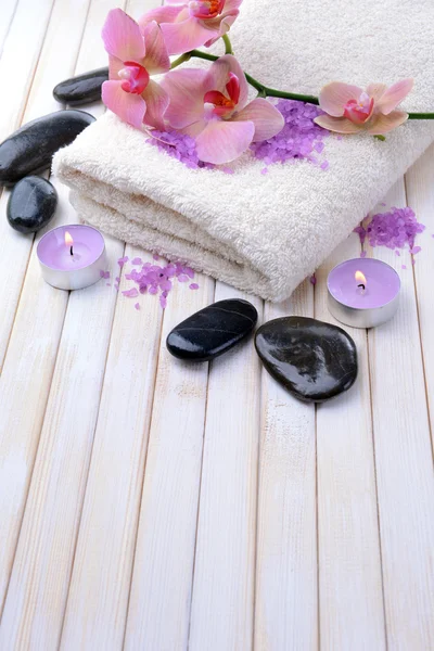 Still life with beautiful blooming orchid flower, towel and bowl with sea salt, on color wooden background — Stock Photo, Image