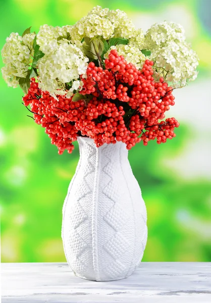 Цветы и ягоды в вазе, на деревянном столе, на ярком фоне — стоковое фото