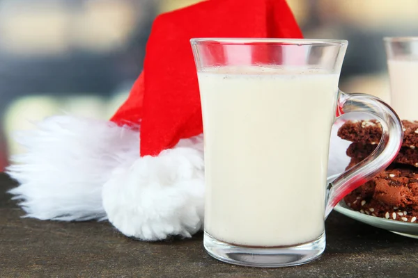 Tasse de lait de poule avec biscuits et chapeau de Père Noël sur la table sur fond lumineux — Photo